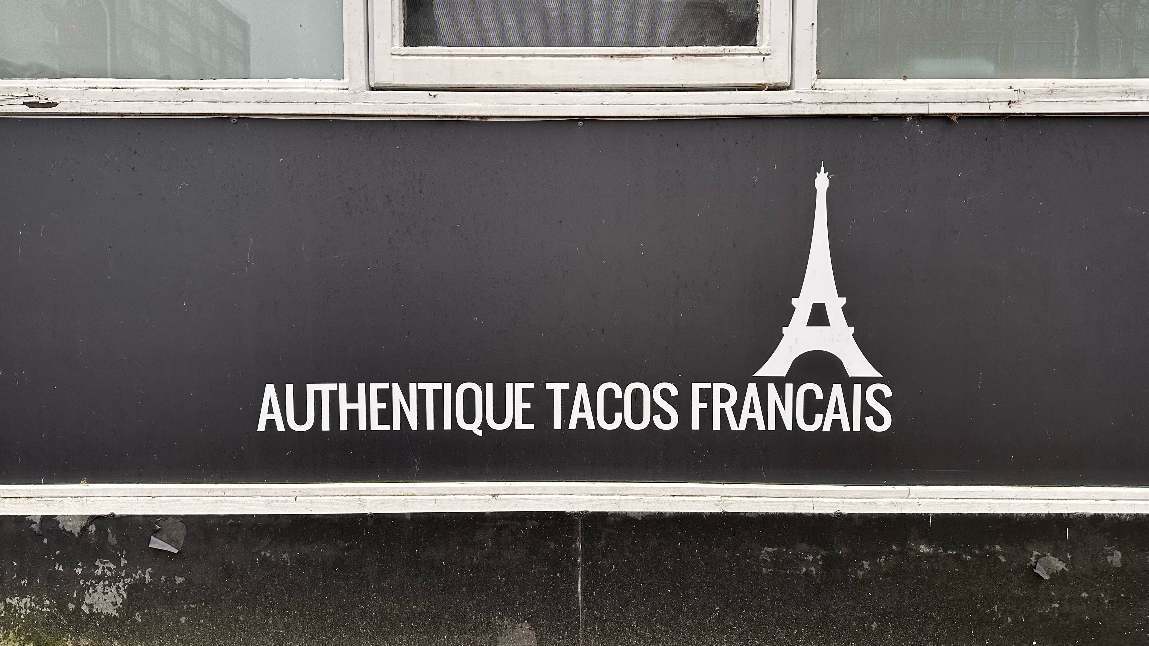 Close up of the Eifel tower logo next to the text authentique tacos Francais. 