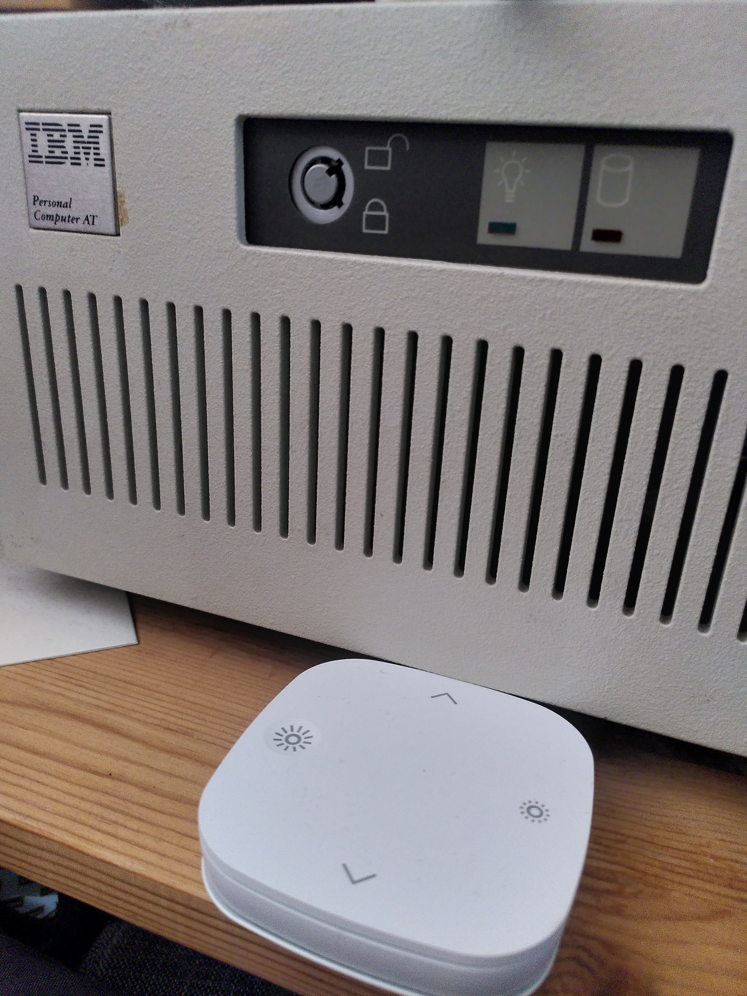 An IBM Personal Computer AT system on a wooden shelf. With an IKEA Tradfri control unit in front of it. The edge of the IKEA unit is squeezed under the front of the IBM.