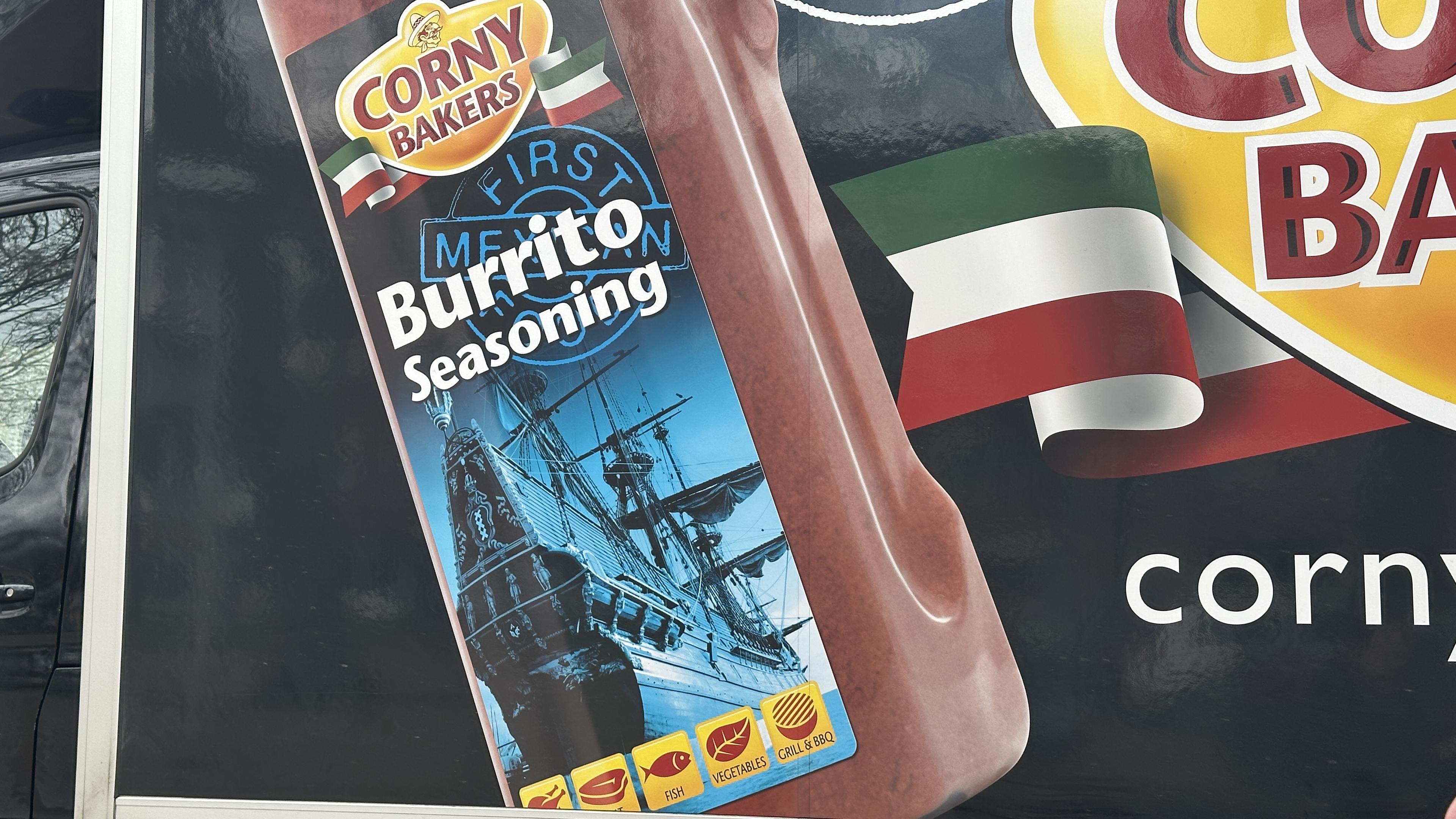 Side of a truck advertising Corny Bakers Burrito Seasoning with a photo of a VOC ship and a cariacature of a Mexican person and a stamp that says First Mexican Food