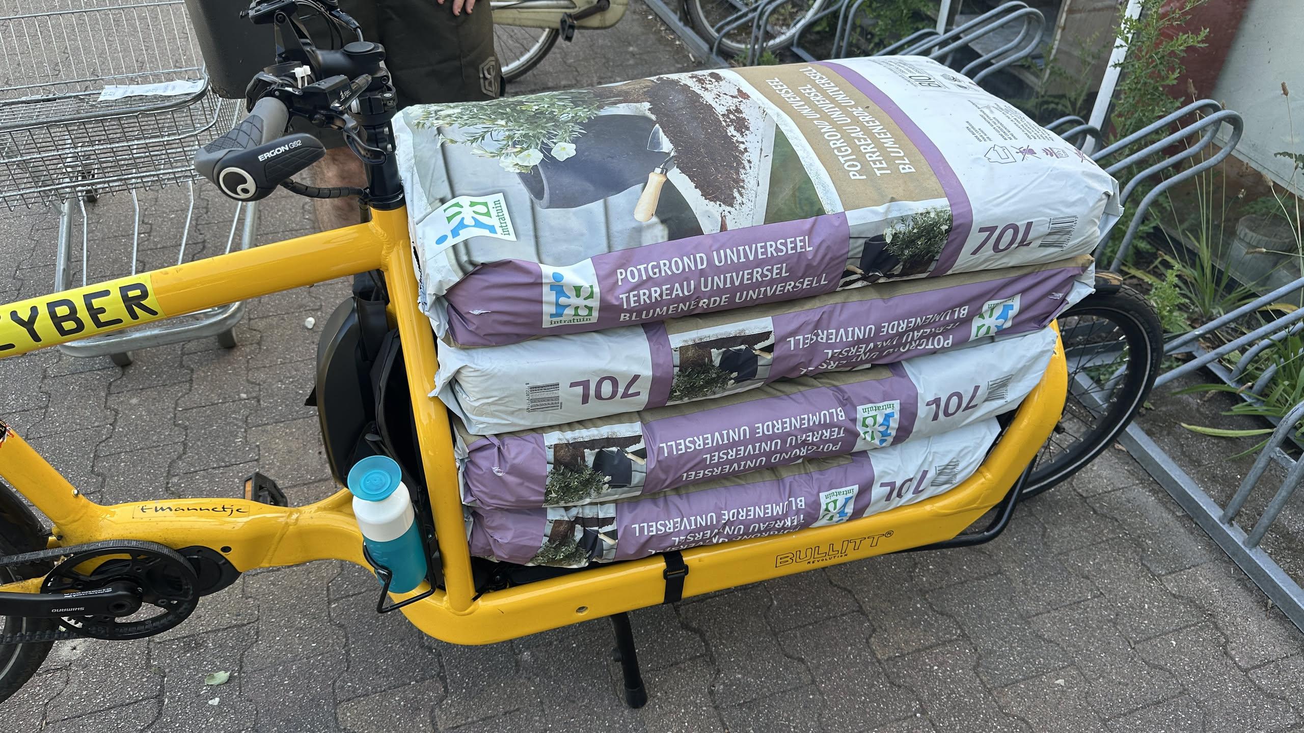 cargo bike loaded with four seventy liter bags of dirt that neatly fit on the narrow flat bed.  it was fine to ride, although you definitely did not want to let it tip too far over when getting on or off.  ratchet straps were added after the photo to secure the load.